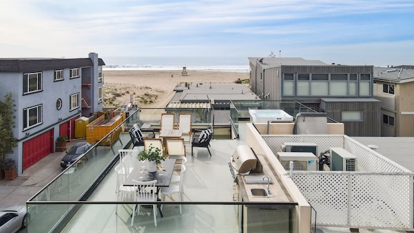 A rooftop terrace with a dining area, outdoor kitchen, and a view of the beach.