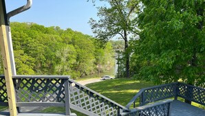 A wooden deck with a lattice railing overlooking a grassy area with trees and a body of water. - Lazy O Resort - 7 bedroom 3 bathroom house. (Camdenton)