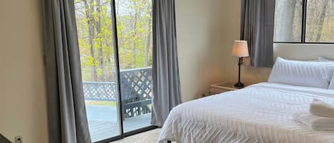A bedroom with a bed, a ceiling fan, and a view of the outdoors through large windows.