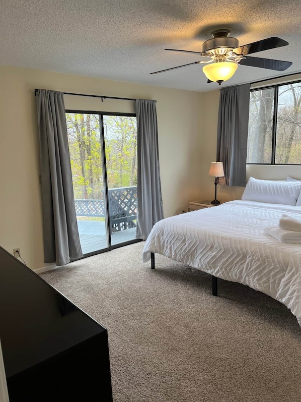 A bedroom with a bed, a ceiling fan, and a view of the outdoors through large windows. - Lazy O Resort - 7 bedroom 3 bathroom house. (Camdenton)