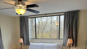 A bedroom with a bed, two bedside tables, a ceiling fan, and a window with curtains. - Lazy O Resort - 7 bedroom 3 bathroom house. (Camdenton)