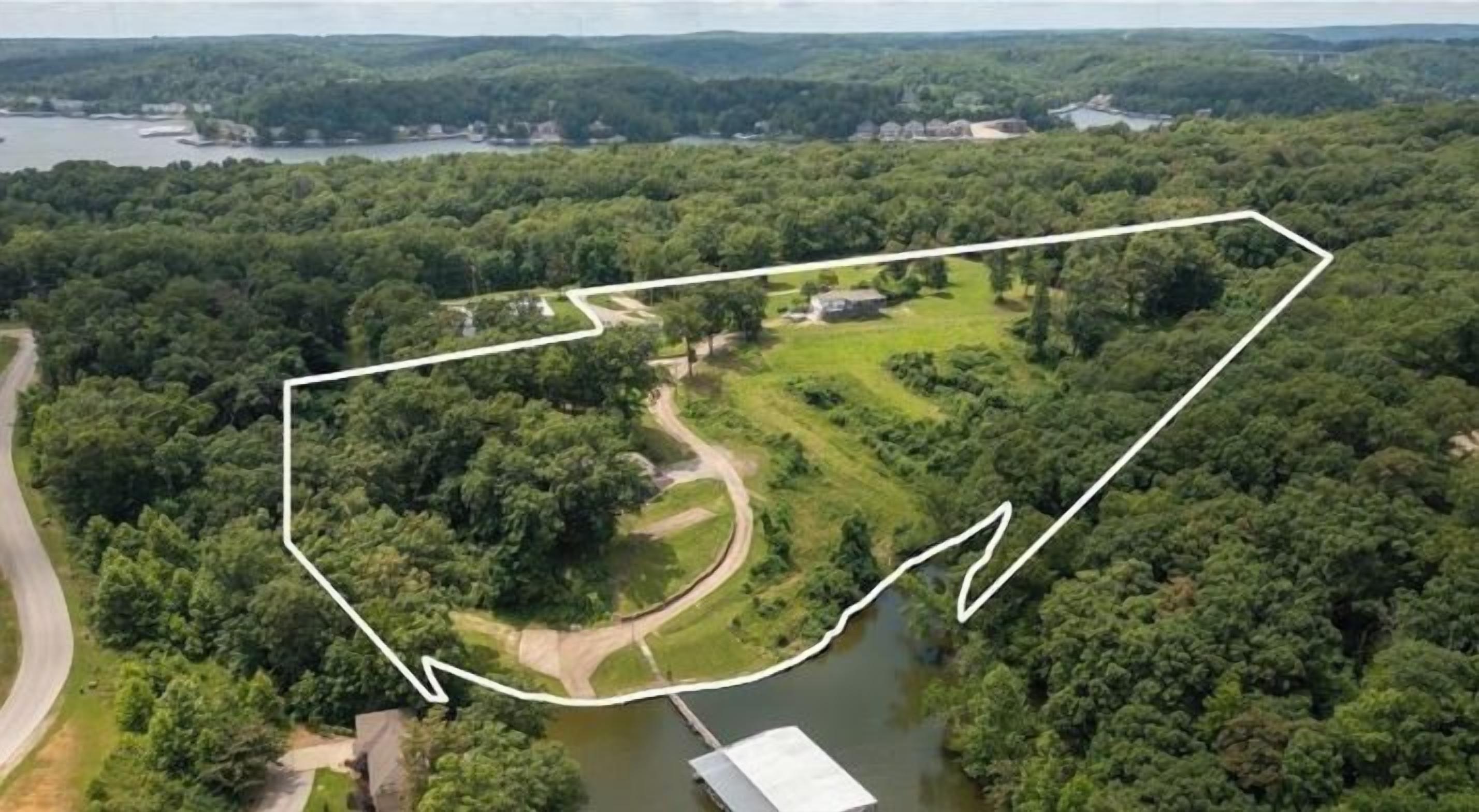 An aerial view of a property with a large green area, a body of water, and a building with a white roof.