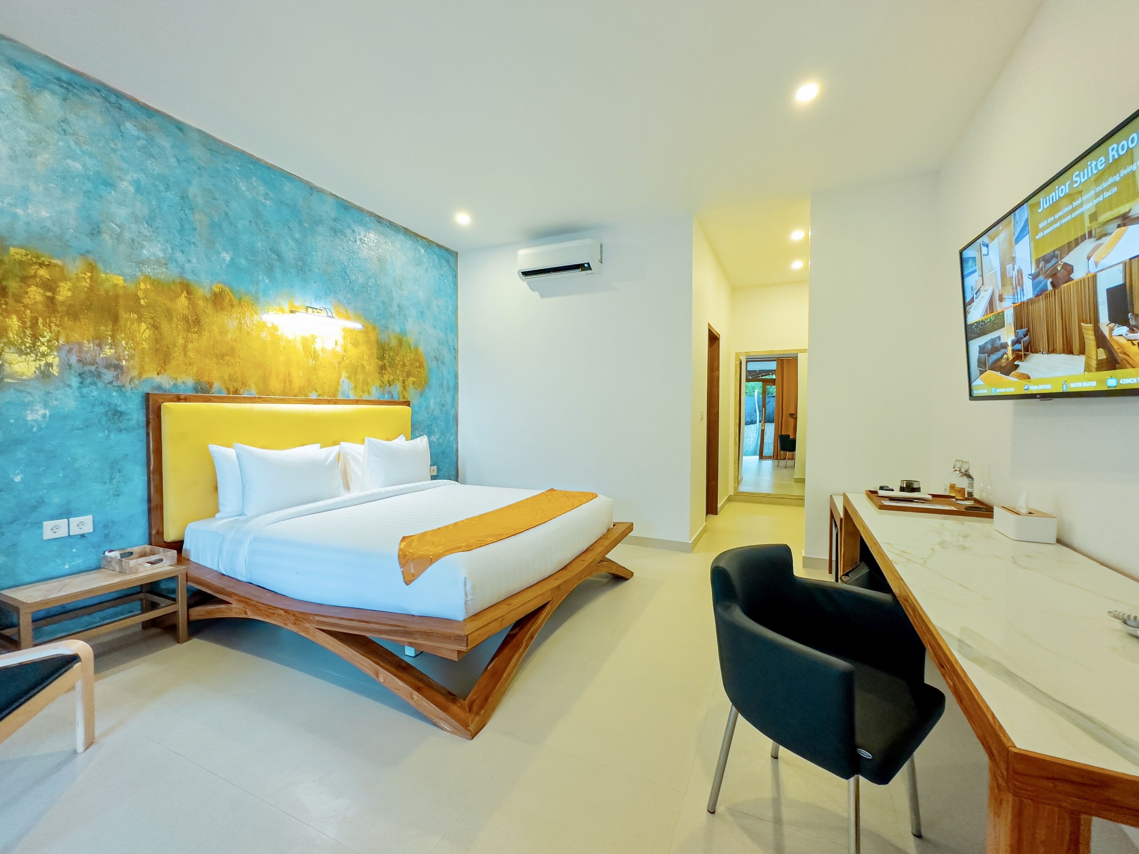 Una habitación de hotel moderna con una cama grande, un escritorio y una silla. Hay un cuadro en la pared y un equipo de aire acondicionado.