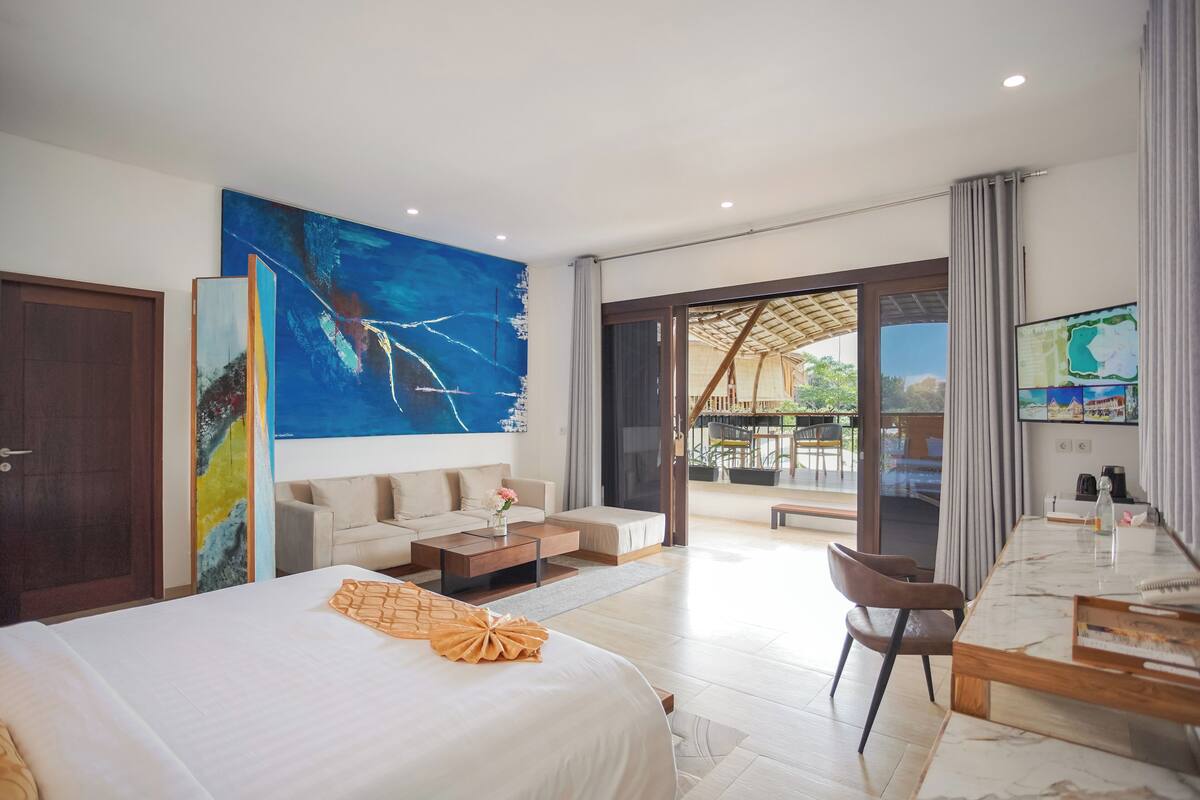 A modern hotel room with a large bed, a sofa, a dining table, and a TV mounted on the wall.