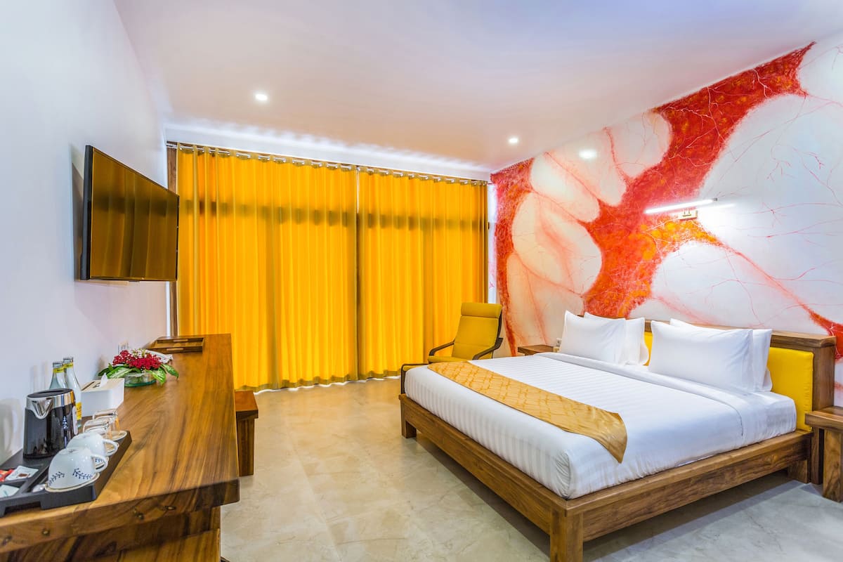 A hotel room with a wooden bed, a desk with a coffee maker, and a TV mounted on the wall.