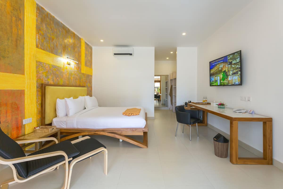 A hotel room with a bed, bedside table, chair, desk, and a television on the wall.