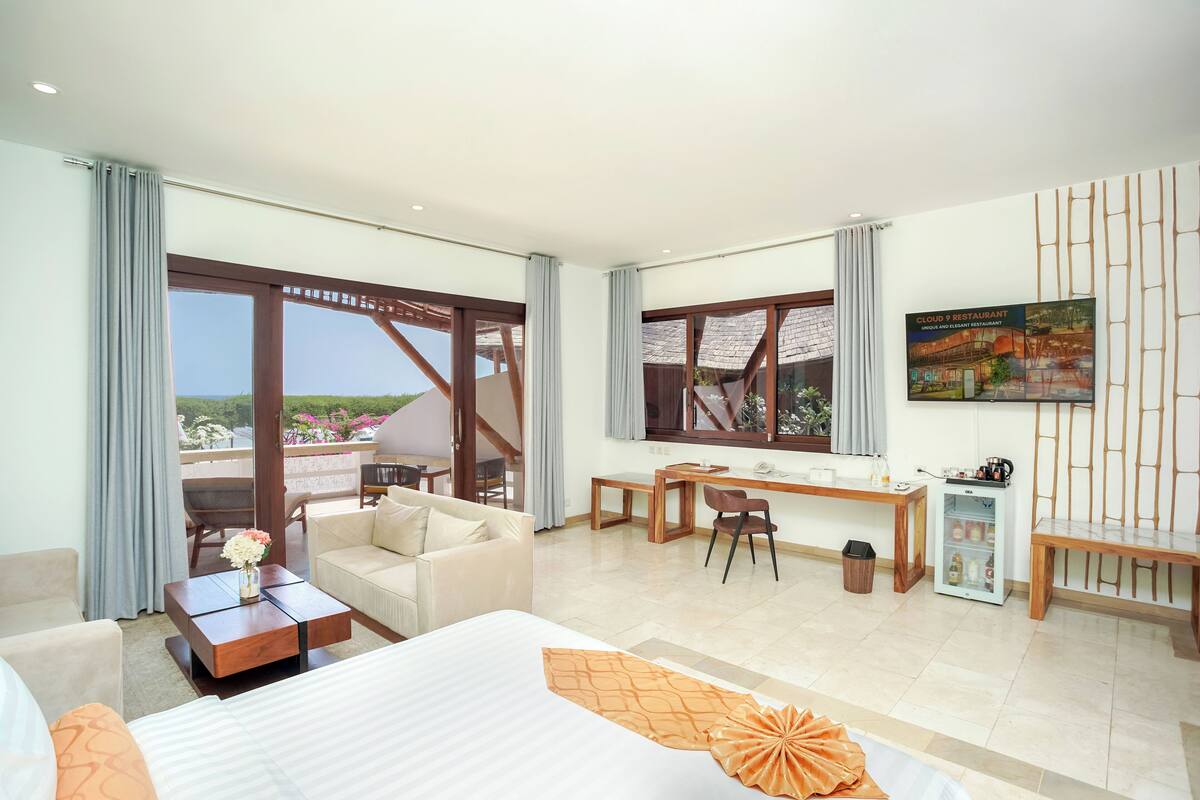 A hotel room with a bed, a desk, a chair, a small table, a sofa, and a balcony with a view.