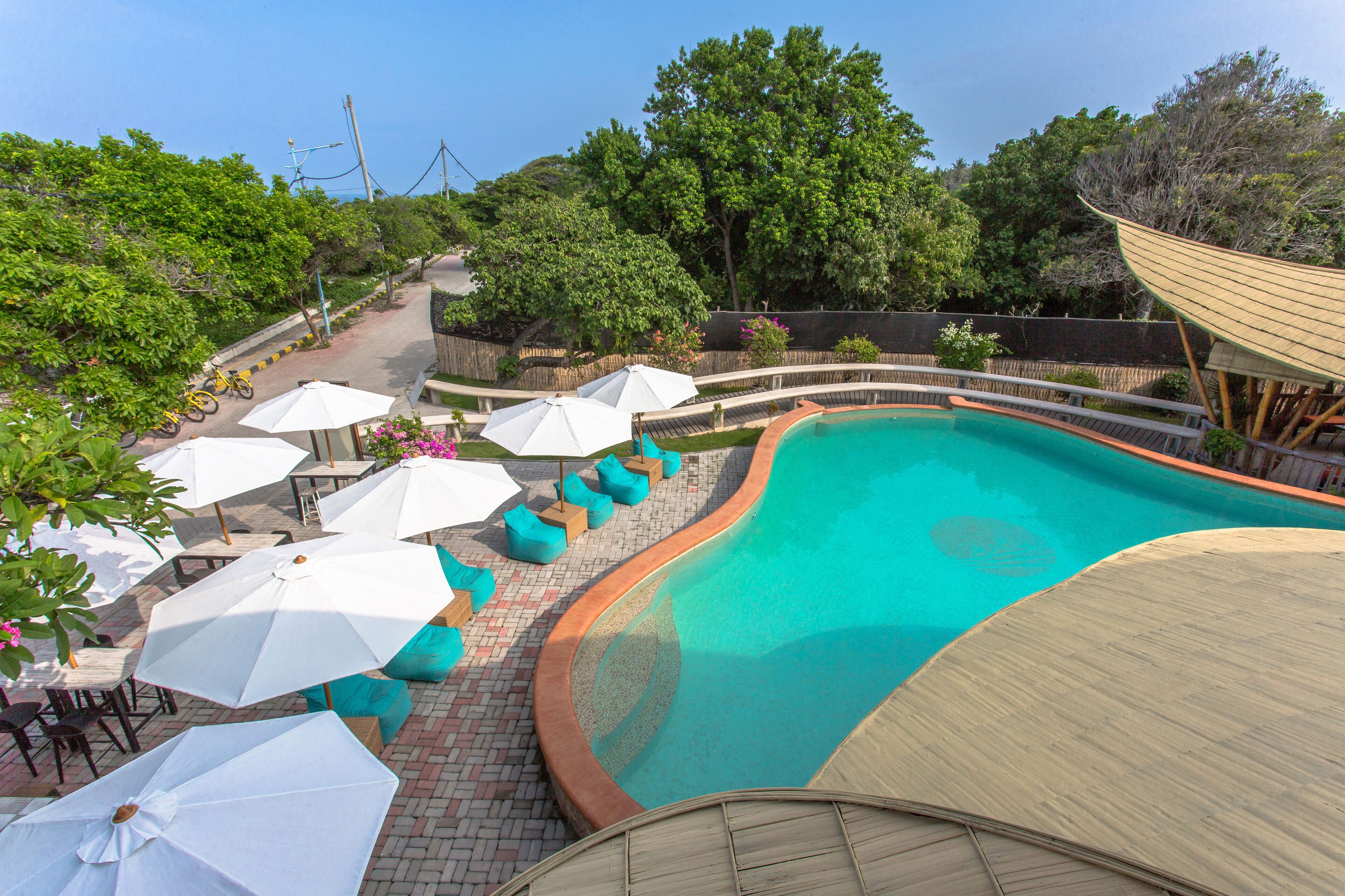 Una piscina de borde curvo, rodeada de sombrillas blancas y asientos color turquesa.