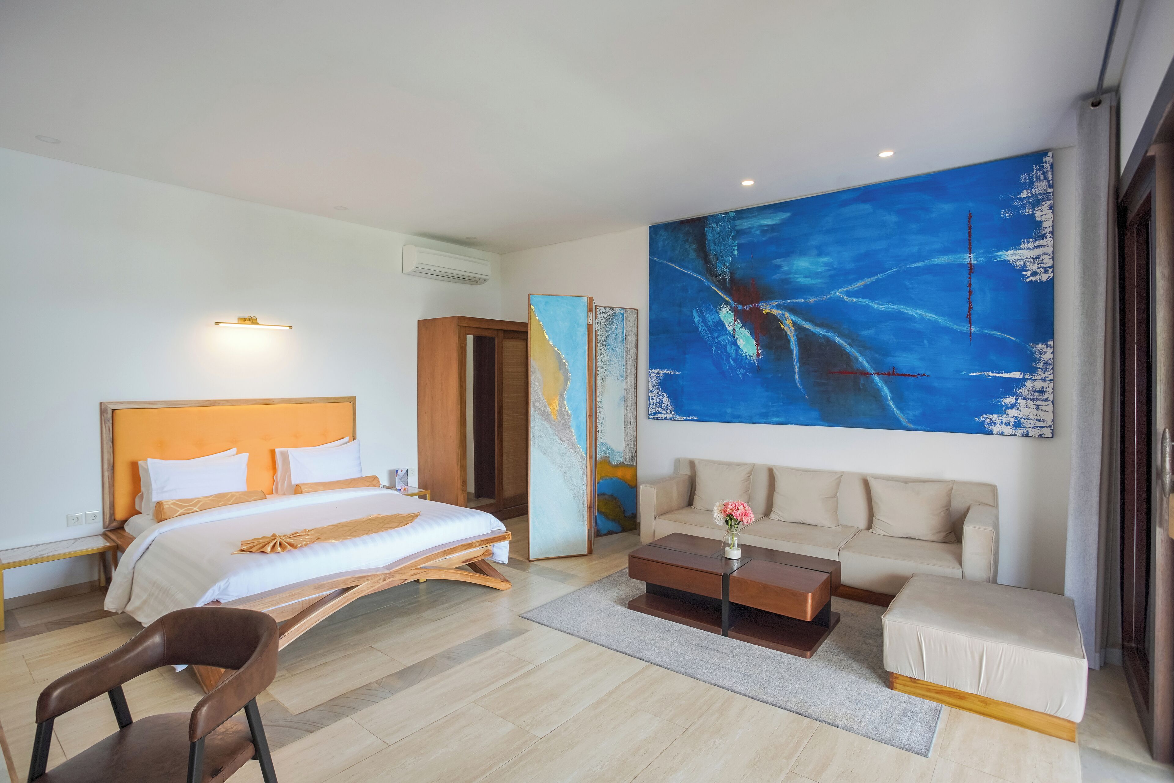 A modern hotel room with a large bed, a sofa, a coffee table, and a painting on the wall.