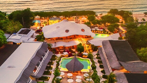 Un resort con piscina, area salotto esterna e vista sull'oceano al tramonto.