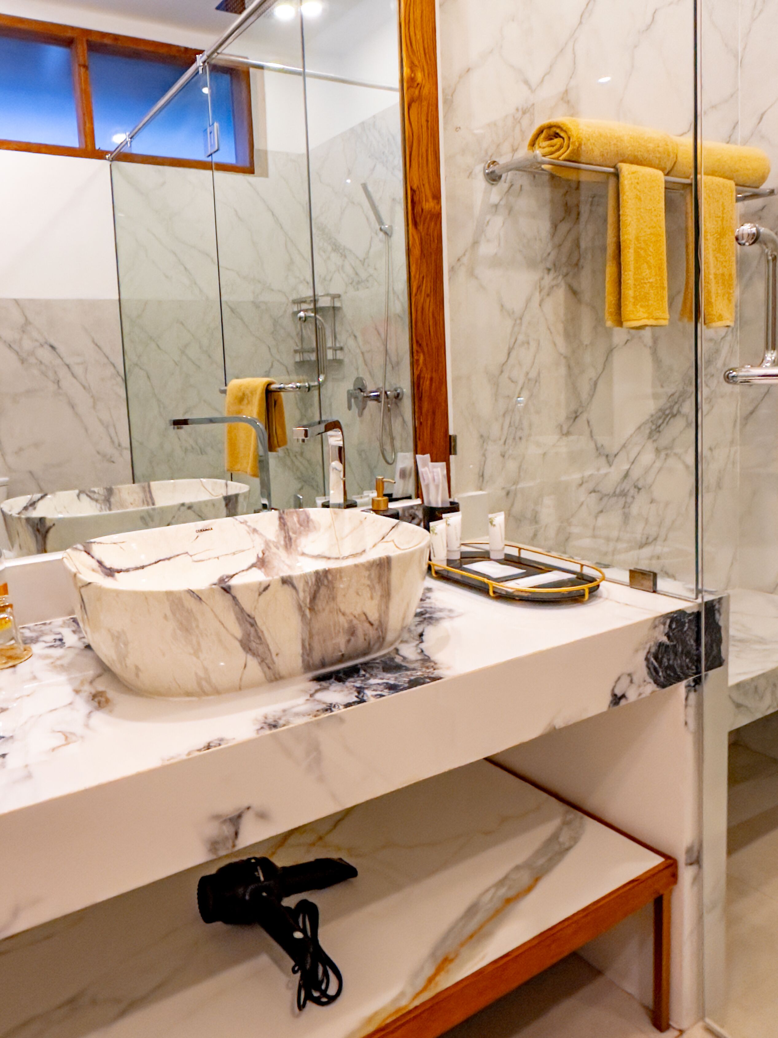 A bathroom with a marble sink, a mirror, and a towel rack with yellow towels.