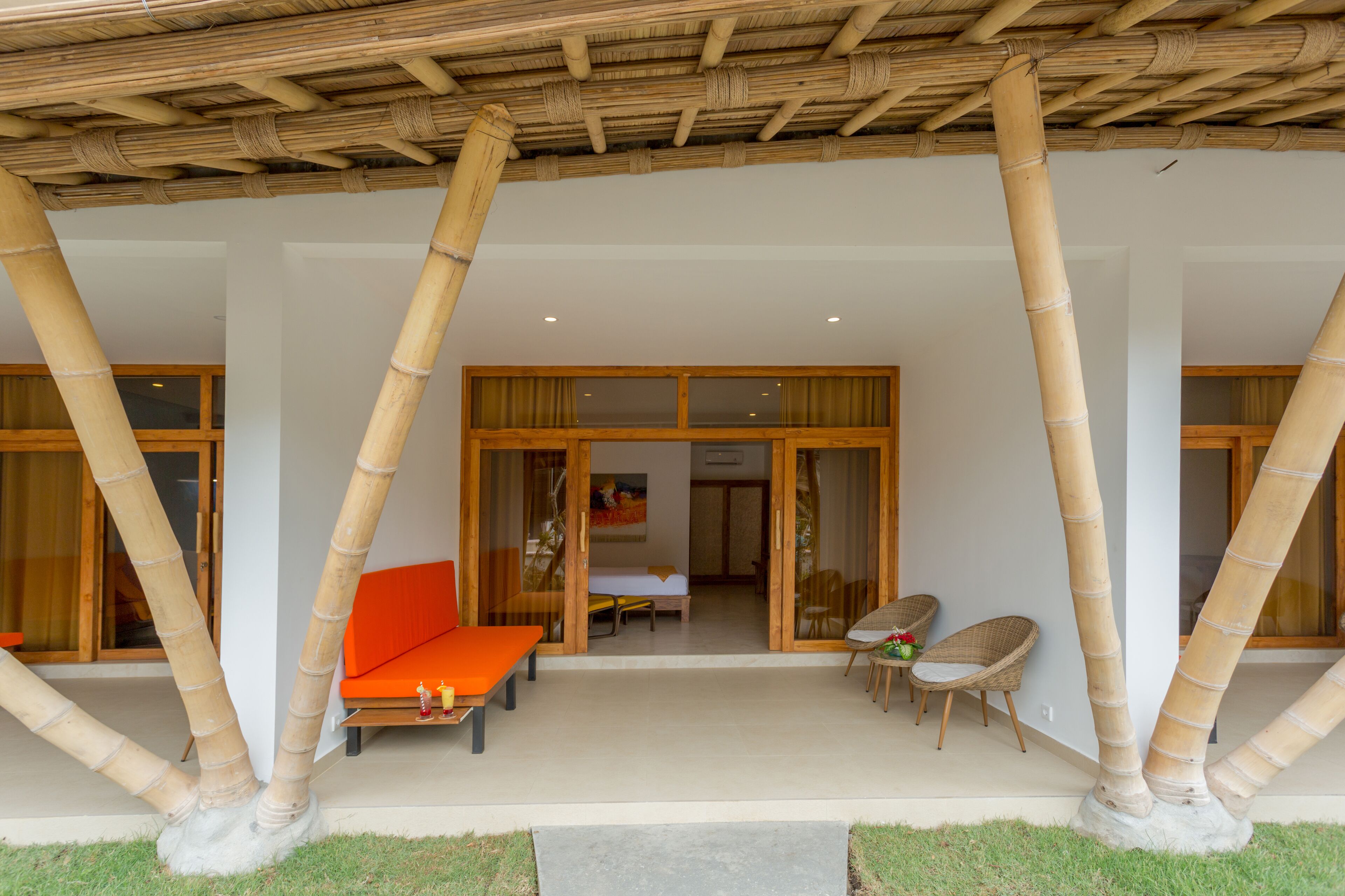 A covered outdoor seating area with bamboo pillars, a sofa, and two chairs.