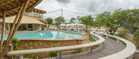 A pool area with a wooden deck, stone walls, and a covered seating area.
