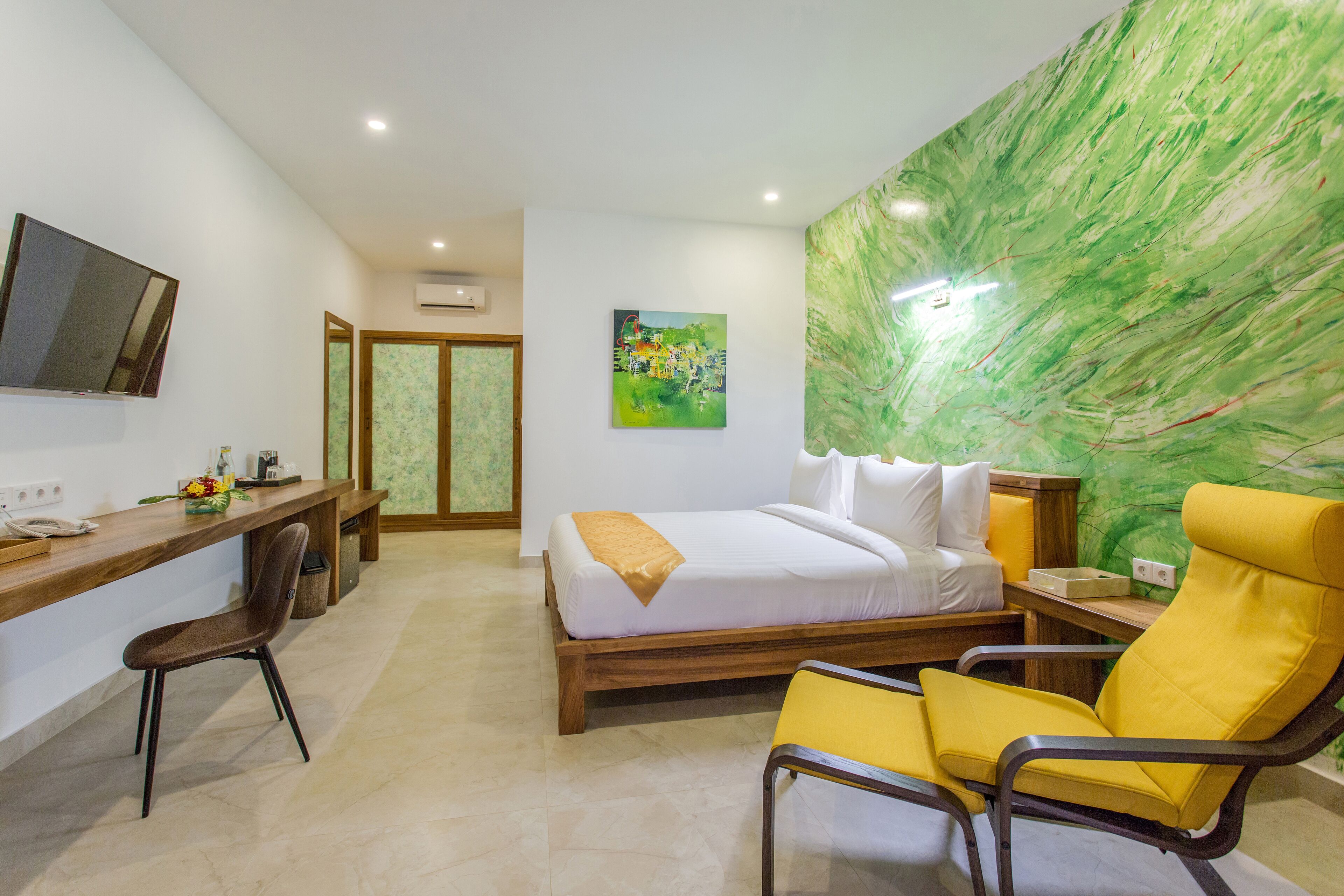 A hotel room with a bed, a desk, a chair, and a large green wall.