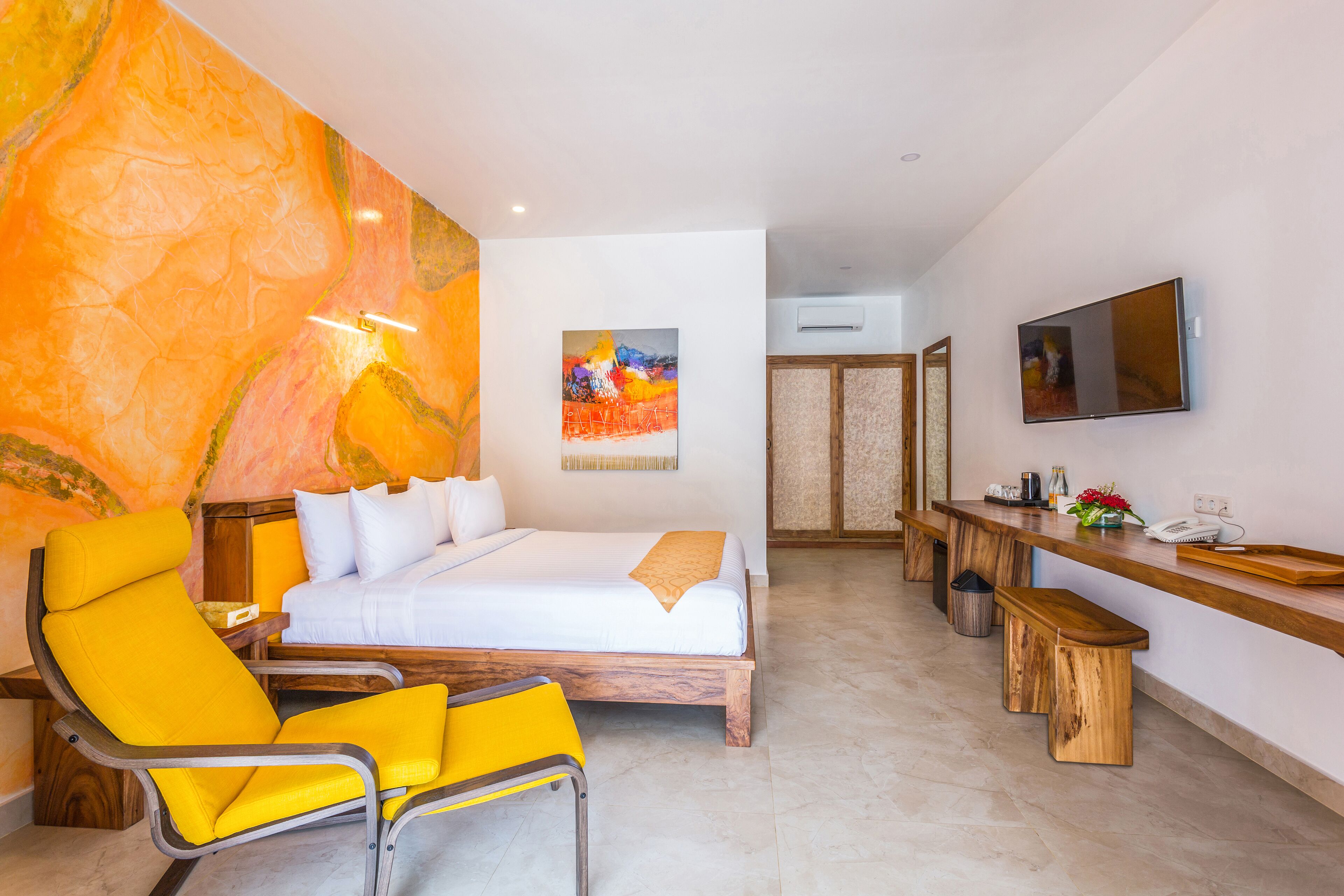 Habitación de hotel con una cama, una silla amarilla, un escritorio de madera, un televisor y un cuadro en la pared.