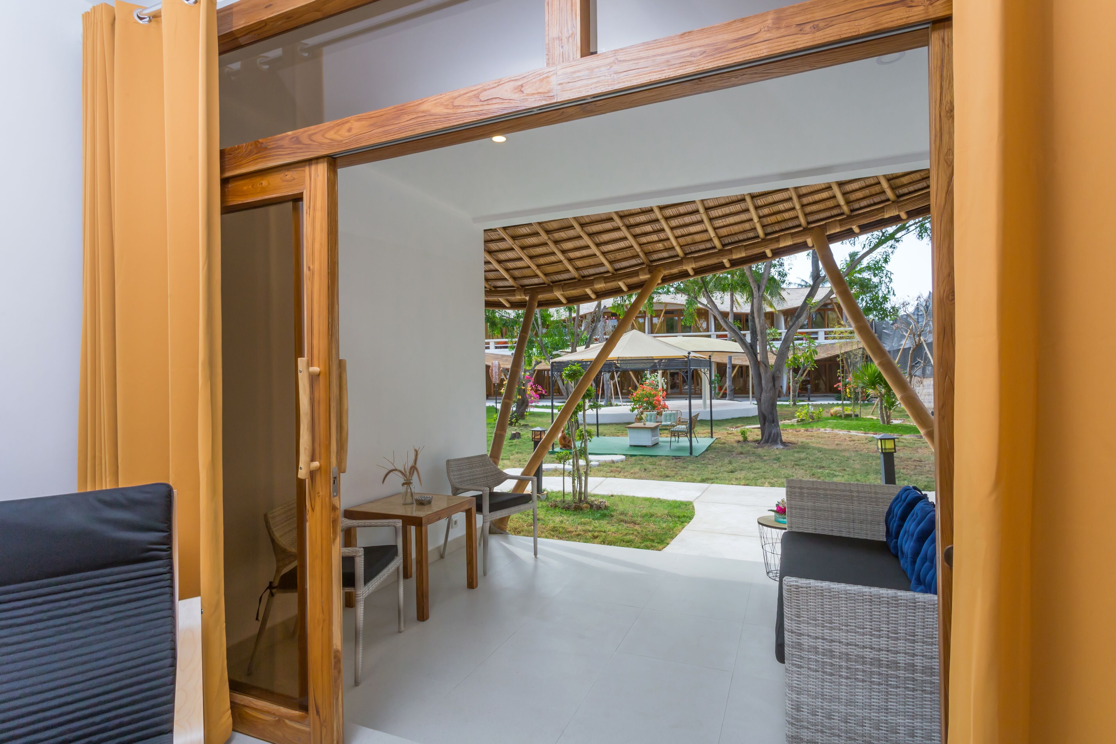 An open-plan living area with a glass door leading to a patio. The patio features a wooden pergola, outdoor seating, and a small garden area.