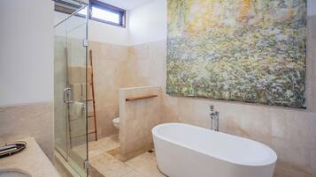Un baño moderno con cabina de ducha de vidrio, una bañera independiente y un cuadro abstracto grande en la pared.