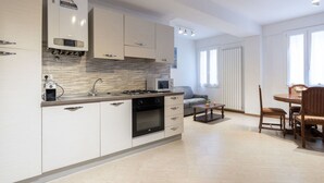 Eine moderne Küche mit weißen Schränken, einem Gasherd und einer Mikrowelle. Es gibt einen Essbereich mit einem Holztisch und Stühlen.