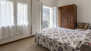 Ein Schlafzimmer mit einem Bett, einem Holzschrank, einem Stuhl und einem Balkon mit Blick ins Freie.