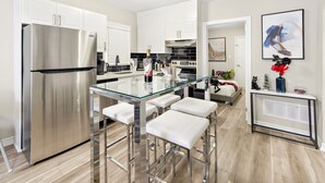 Una cucina moderna con elettrodomestici in acciaio inossidabile, un'isola con piano in vetro e sgabelli da bar, e un'area pranzo con tavolo e sedie bianche.