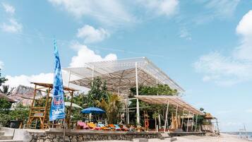 Un resort frente a la playa con una amplia estructura al aire libre, una bandera y sillas de playa.