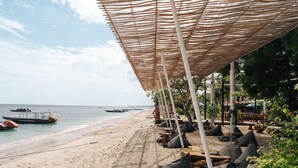 Un área de descanso en la playa con sombrillas y cojines, con vista al mar.