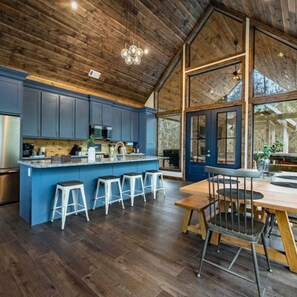 Een moderne keuken met blauwe kastjes, een centraal eiland met krukken en een groot raam met uitzicht op een natuurlandschap.