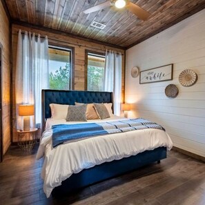 Ein Schlafzimmer mit einem großen Bett, Holzboden und zwei Fenstern mit Vorhängen.