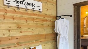Un mur en bois orné d’une pancarte « Bienvenue », un banc avec des coussins et un peignoir suspendu à un porte-manteau.