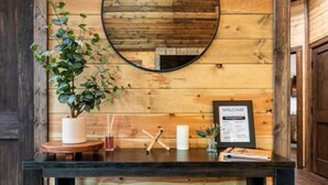 A wooden wall with a round mirror, a welcome sign, and a small wooden box on a black console table. - Luxury Cabin! Hot tub, Pet Friendly, Foosball! (Broken Bow)