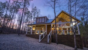 A wooden cabin with a glass front, surrounded by trees. - Luxury Cabin! Hot tub, Pet Friendly, Foosball! (Broken Bow)