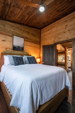 Ein Schlafzimmer einer Holzhütte mit einem großen Bett, einem Deckenventilator und einem Nachttisch mit Lampe.