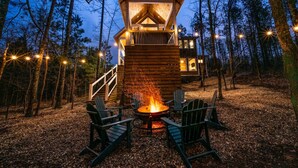 A wooden cabin with a fire pit and chairs in a forest setting. - Luxury Cabin! Hot tub, Pet Friendly, Foosball! (Broken Bow)