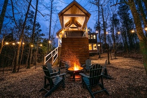 Une cabane en bois avec un foyer et des chaises, située dans un cadre forestier.