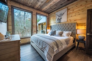 Une chambre avec un grand lit, des murs en bois, une fenêtre et une vue sur les arbres.