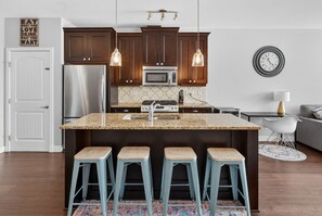 Una cocina con una isla central, taburetes de bar, un refrigerador, un microondas y lámparas colgantes.