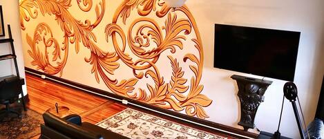 A living room with a decorative wall, a ceiling fan, a flat-screen TV, and a black leather sofa.