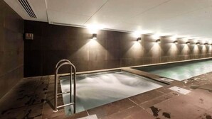 Una piscina interior larga con una escalera metálica, paredes de azulejos y luces empotradas.