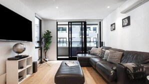Una sala de estar moderna con un sofá de cuero negro, un mueble blanco para el entretenimiento y un televisor de pantalla plana grande.