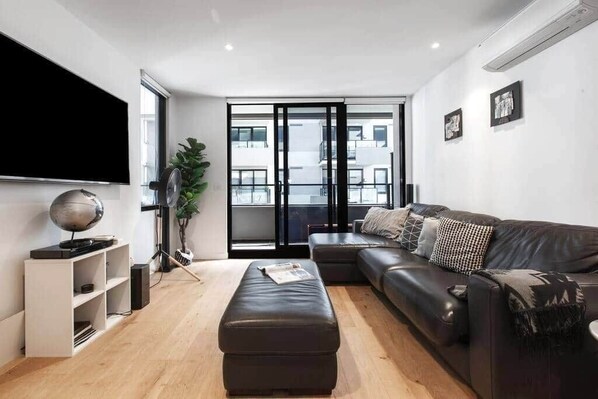 Una sala de estar moderna con un sofá de cuero negro, un mueble blanco para el entretenimiento y un televisor de pantalla plana grande.