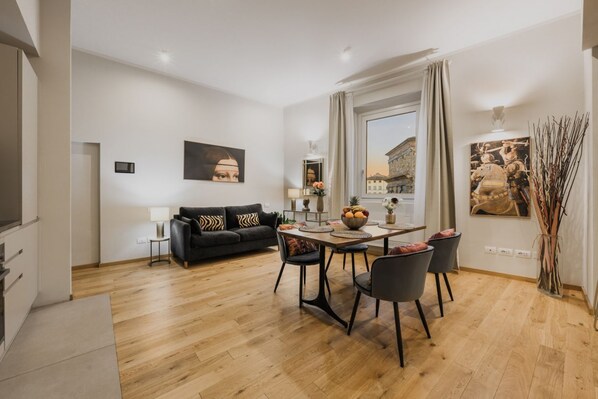 Una sala de estar moderna con comedor, un sofá negro, una mesa con sillas y una ventana con vistas a edificios.
