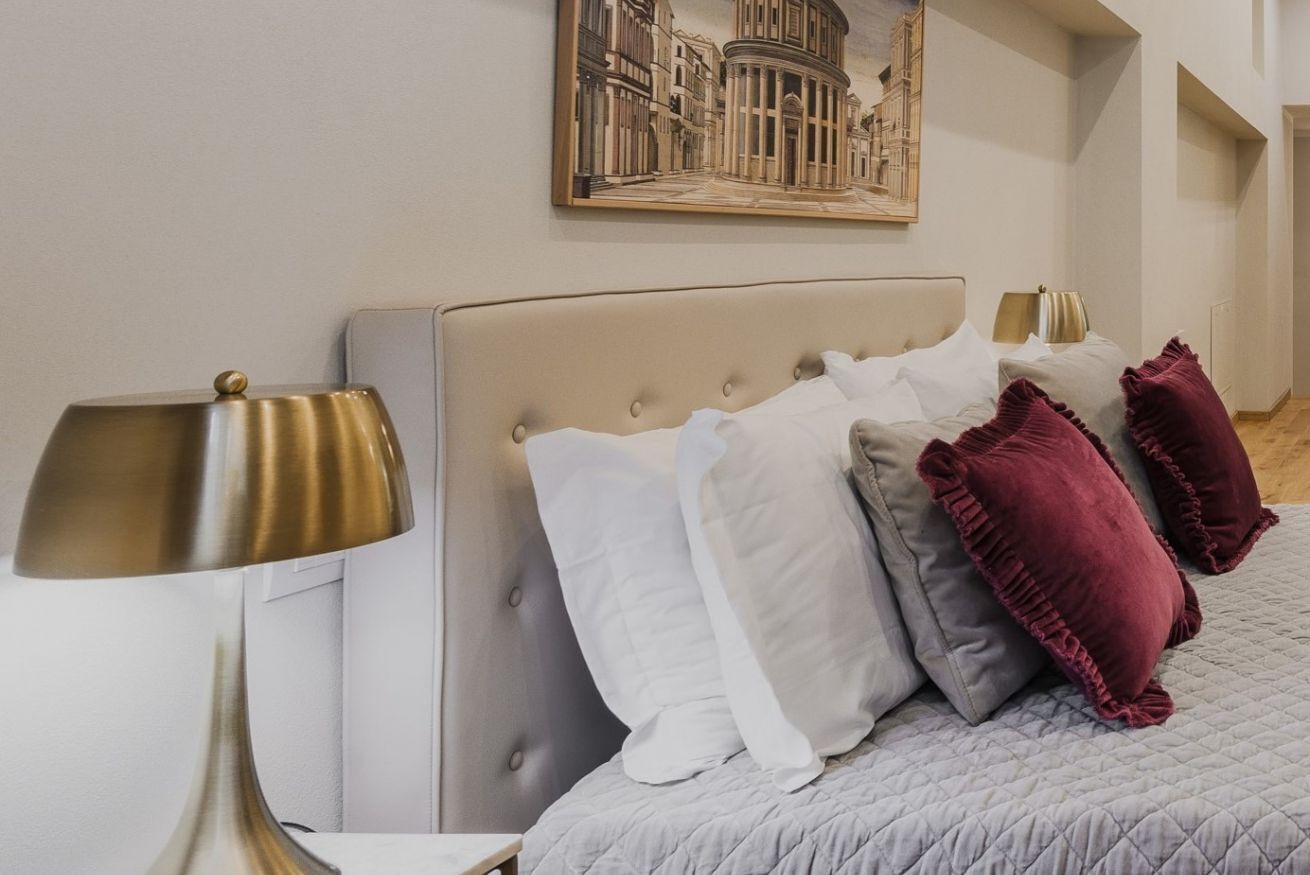Un lit bien fait, avec une tête de lit capitonnée, une lampe de chevet et un tableau encadré au mur.
