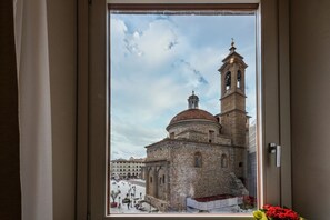 Une vue à travers la fenêtre d’un bâtiment historique doté d’un clocher et d’un dôme, d’une cour et d’un ciel dégagé.