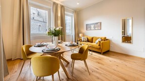 Ein modernes Wohnzimmer mit Esstisch, gelben Stühlen, einer Couch und einem großen Fenster mit Vorhängen.
