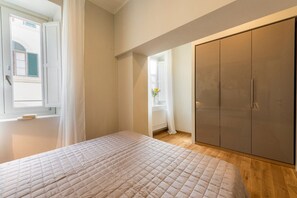 A bedroom with a bed, a wardrobe, a window with curtains, and a view of a building outside.