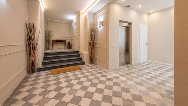 Eine Hotelhalle mit Schachbrettmuster-Boden, einer Treppe und einer Tür zu einem Aufzug.