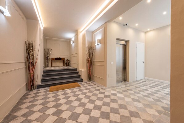 A hotel lobby with a checkered floor, a staircase, and a door leading to an elevator.