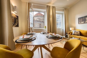 Comedor con una mesa redonda, sillas amarillas y vista a un edificio a través de una ventana.