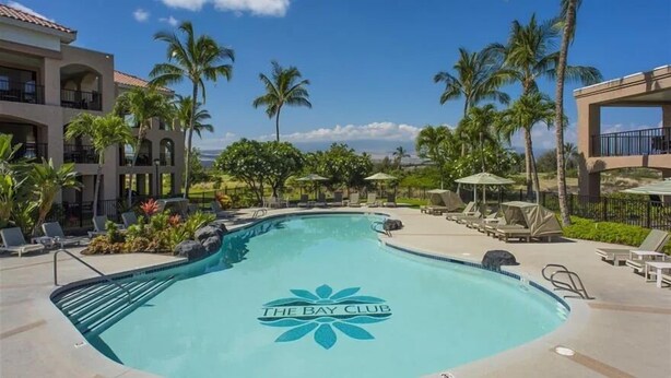A swimming pool with a logo at the center, surrounded by lounge chairs and palm trees.
