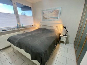 A bedroom with a bed, a nightstand, a lamp, a window, and a painting on the wall.
